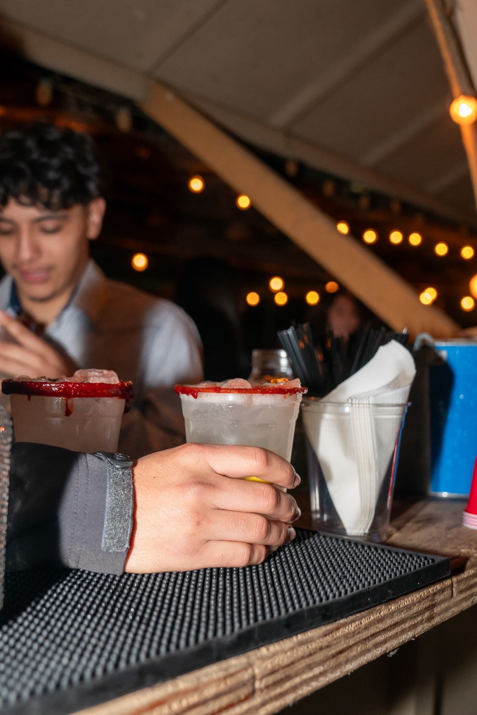 Rimdrip bartender at twilight serving micheladas under string lights